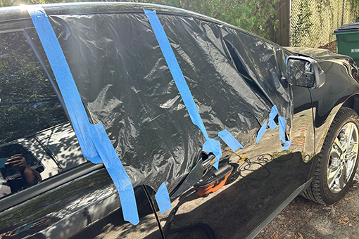 Car Window In Need of Auto Glass Repair Services Covered With Plastic While Parked at Riverview Residence